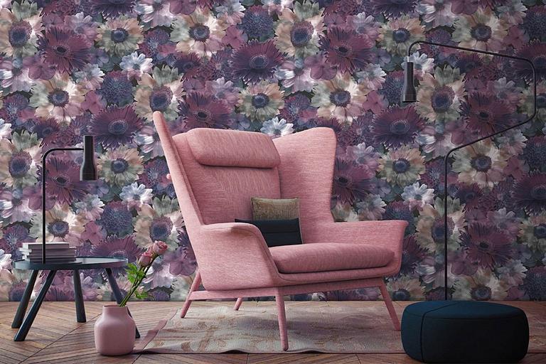 A pink chair in front of a floral wallpapered wall.