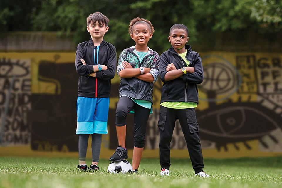 Three children, all wearing a Garmin vivofit Jr. 3 fitness tracker, pose with a football.