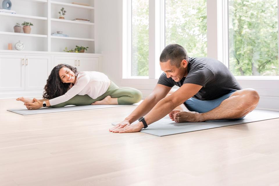 Two people do yoga stretches in a light-filled white room, wearing Garmin smartwatches.