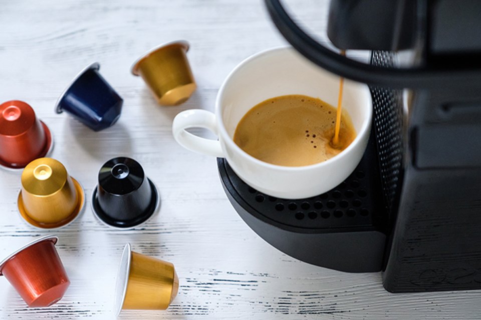 Coffee pods near a coffee machine expressing coffee in a white mug.