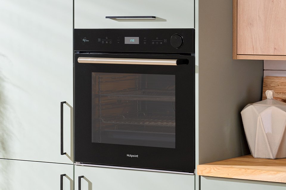 Hotpoint black oven seamlessly built into modern green kitchen cabinets.