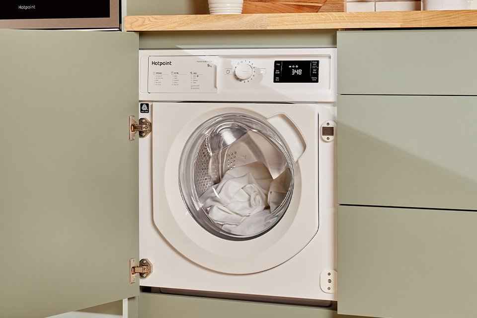 Hotpoint white tumble dryer seamlessly built into modern green kitchen cabinets.