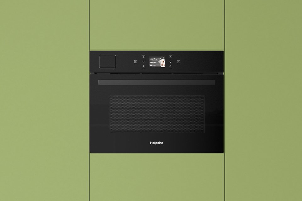 Hotpoint black microwave built into modern green kitchen cabinets.