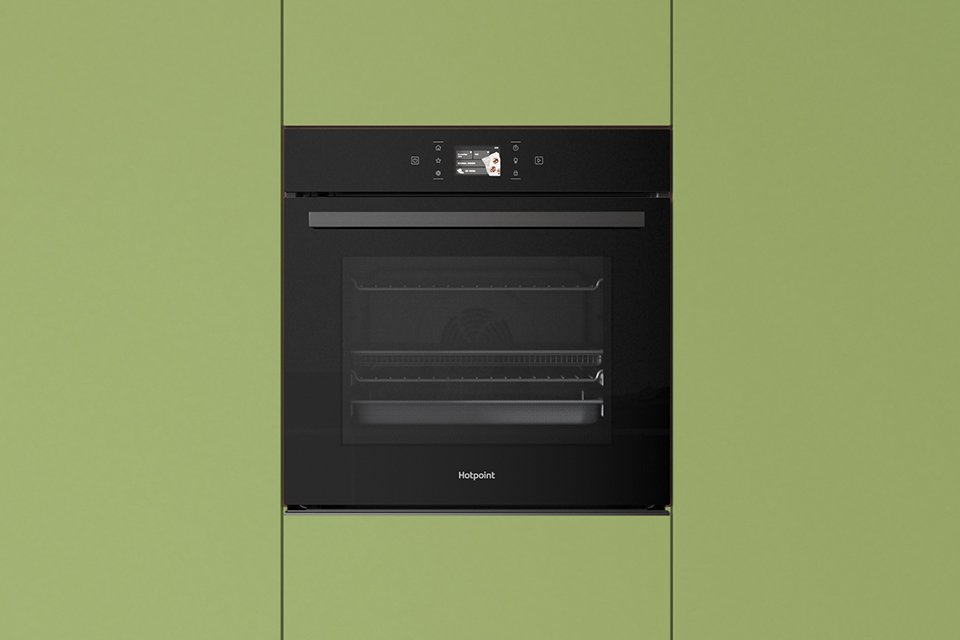 Hotpoint black oven built into modern green kitchen cabinets.