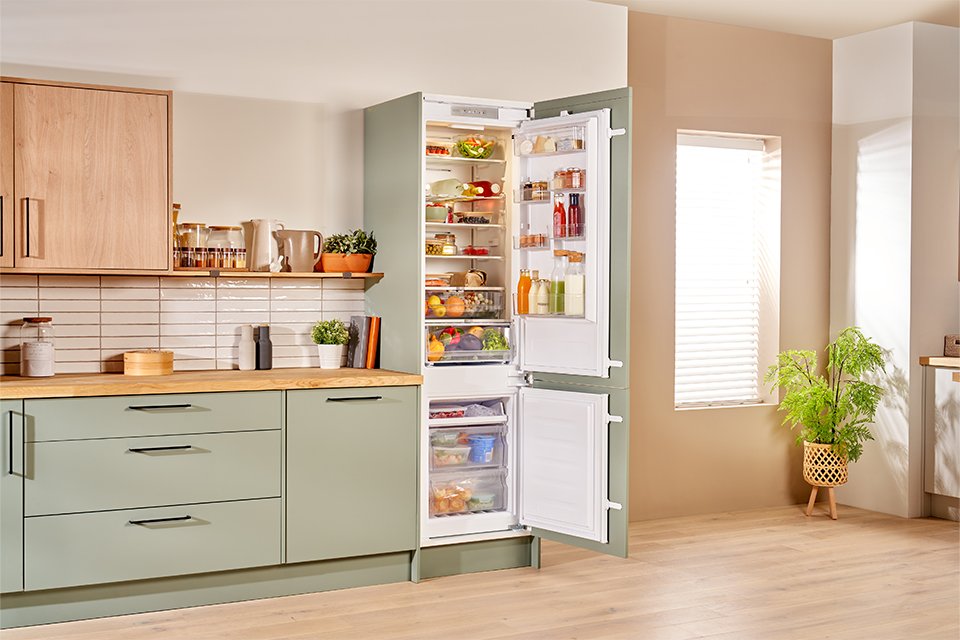 Hotpoint white fridge freezer seamlessly built into modern green kitchen cabinets.