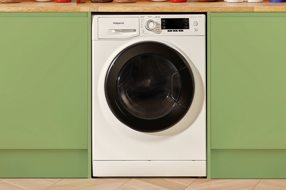 A Hotpoint white washer dryer seamlessly built into modern green kitchen cabinets.