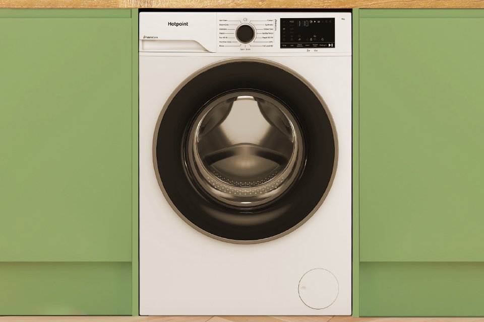 A Hotpoint white washing machine seamlessly built into modern green kitchen cabinets.