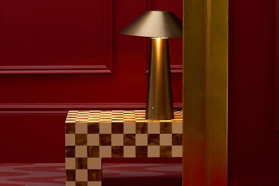 A gold Habitat table lamp on top of a chequered coffee table placed in a hotel lift.