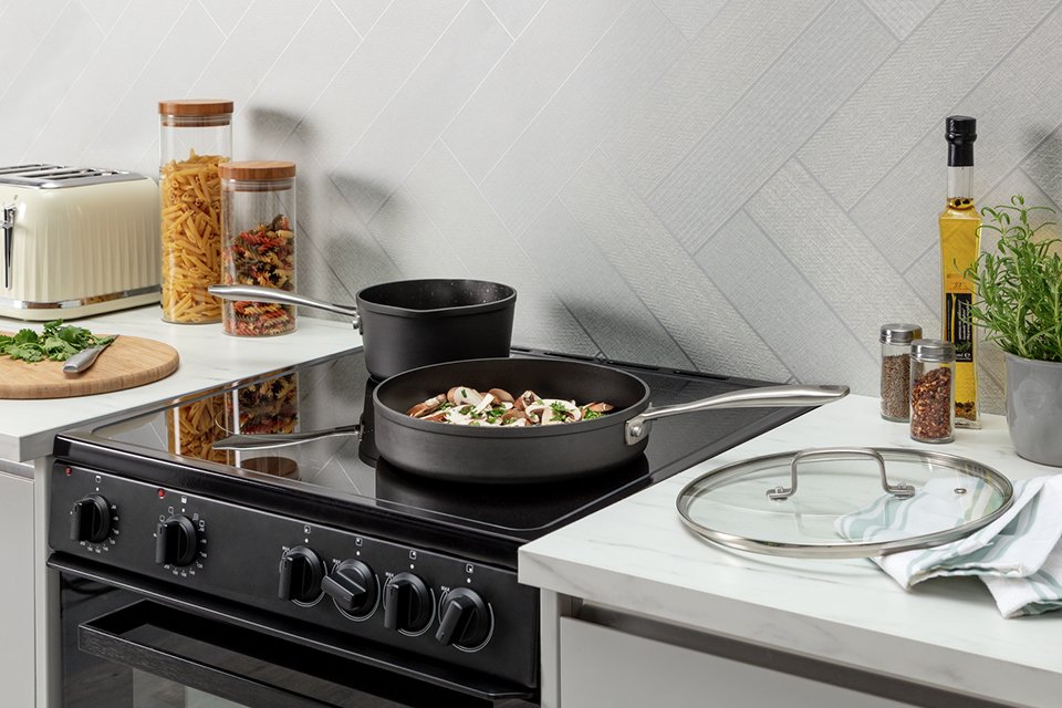 A Habitat sauté pan on the stove with some food cooking in it.