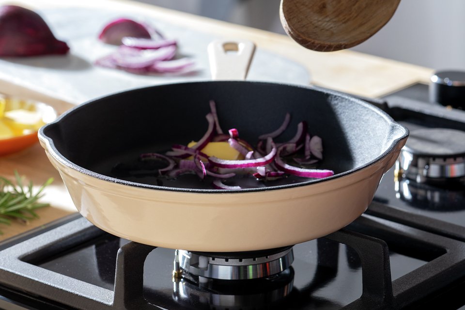 A person cooking with the Habitat cast iron frying pan with enamel coating.