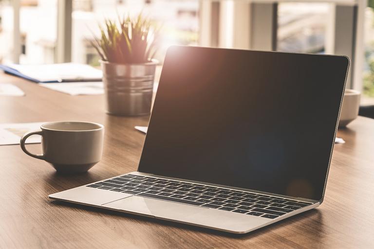 A coffee or tea cup near a laptop on a work table.