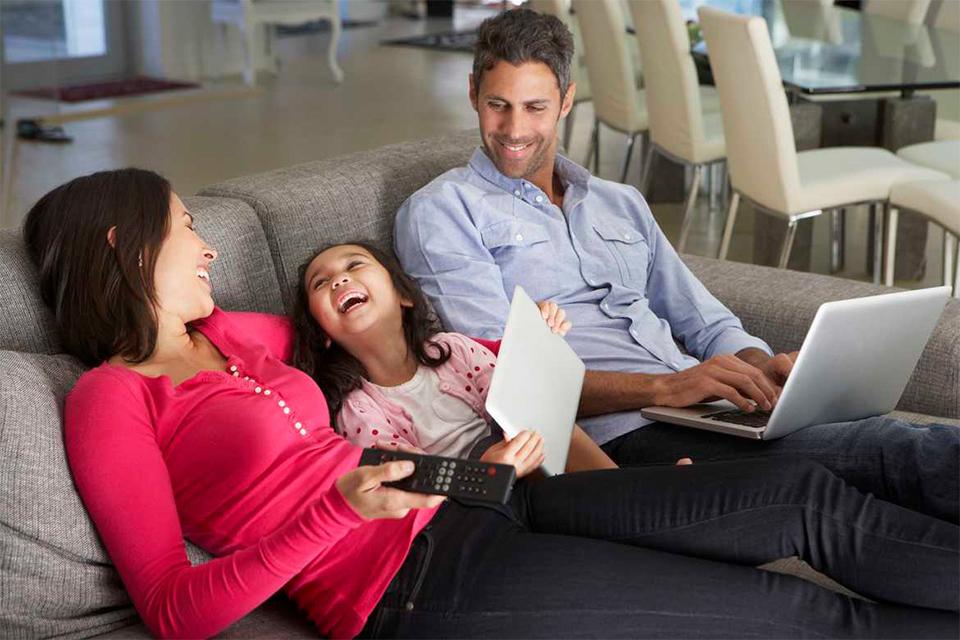 A family of 3 laughing while they are using different devices to get entertained.