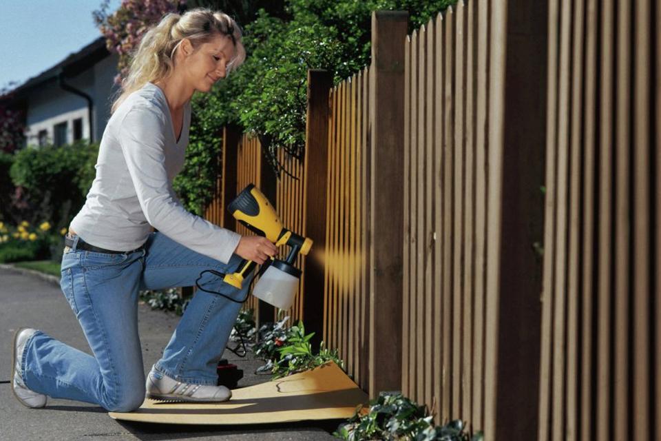 Woman spray painting a fence brown.