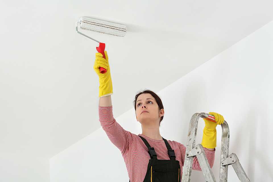 Woman on step ladder painting ceiling white with roller.