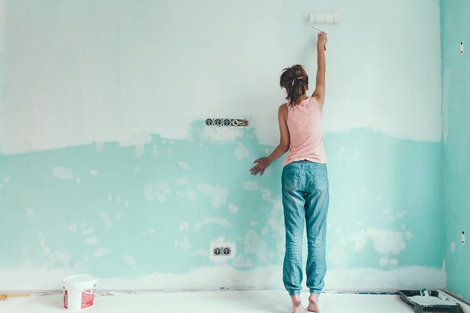 Woman using a roller to paint a wall duckegg.