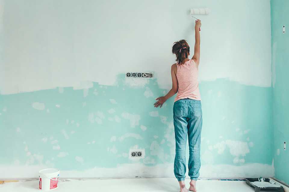 Woman using a roller to paint a wall duckegg.