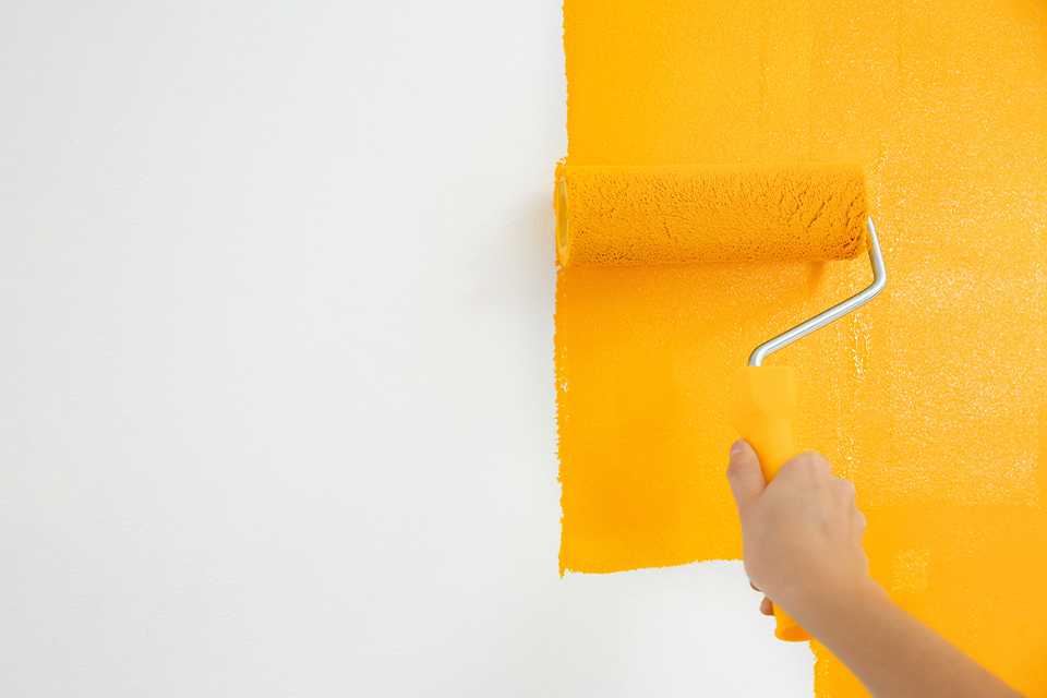 Person using a roller to paint a wall yellow.