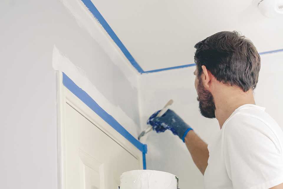 Man cutting in white paint around doorframe.
