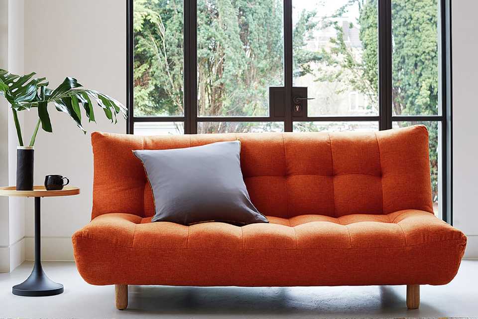The orange Habitat Kota sofa with a large grey cushion on it.