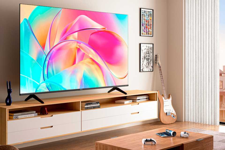 A Hisense U8H Mini-LED 4K HDR TV stood on a TV unit next to a vase, in a living room.