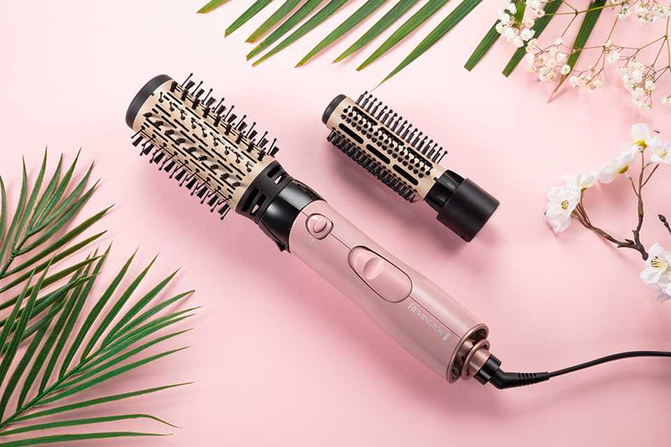 Light pink Coconut Air Styler with rose gold accent and additional brush attachment on a pink background with tropical leaves.
