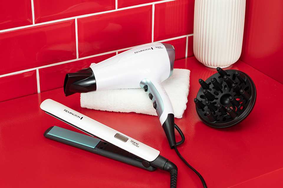 White and teal Shine Therapy hair straighteners and hair dryer with diffuser on a red countertop with red tiled wall behind.