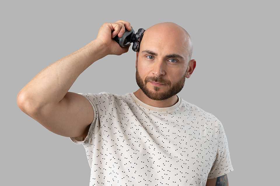 Man holding the RX7 head shaver to his bald head using it to achieve a skin close shave.