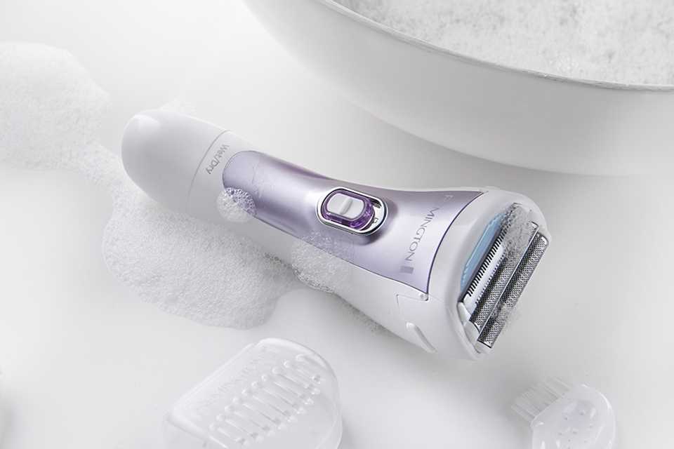 Cordless Lady Shaver wet with soapy bubbles placed on a white countertop next to a full sink.