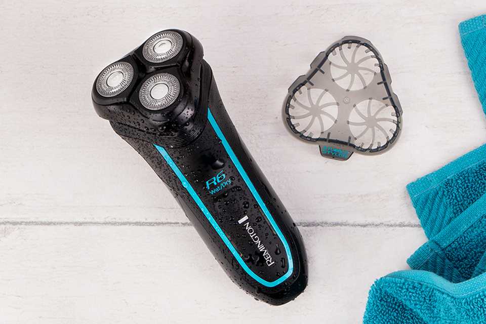Black rotary shaver with bright blue accents on a wooden backdrop with shaver guard and a towel in frame.