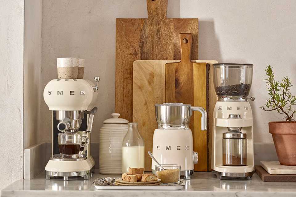A cream coloured Smeg espresso coffee machine, milk frother and coffee grinder.