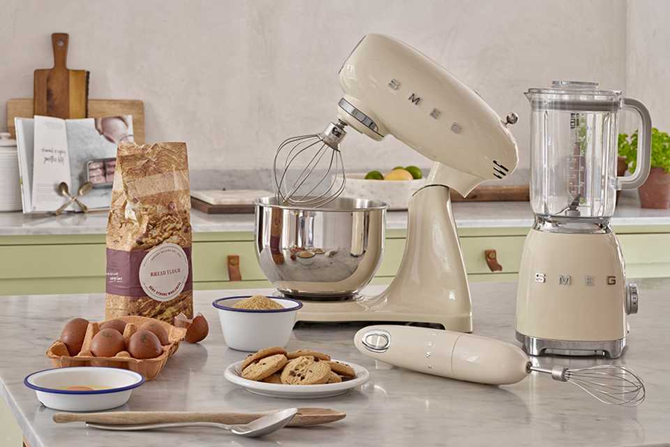 A cream coloured Smeg stand mixer, blender and hand blender placed on a slab.