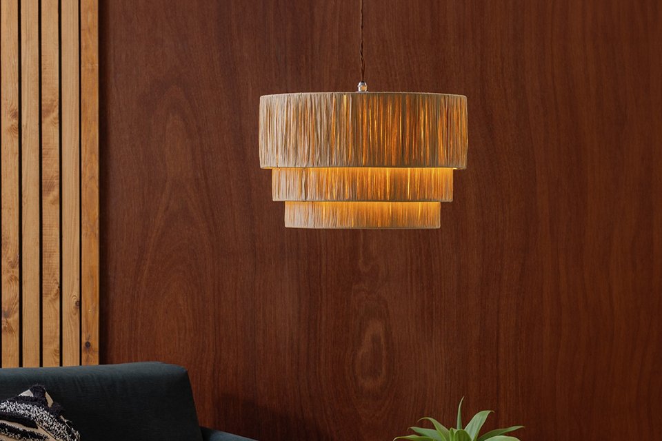 Habitat Salto Beige Rattan 3 Tier Pendant Shade hung over an armchair in a living room.