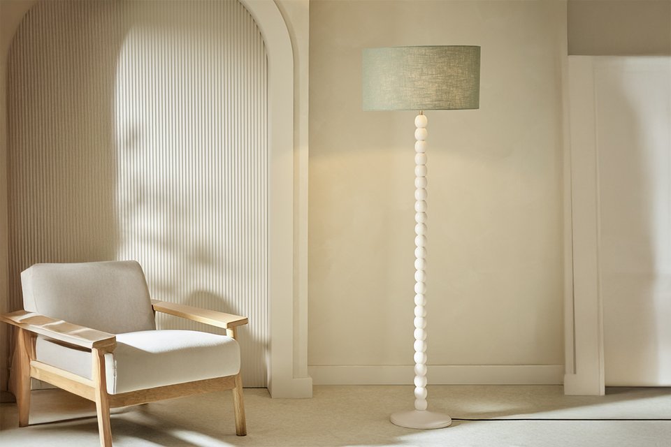 A Habitat Bobbin Mango Wood Floor Lamp Base Only - Ivory near an armchair.