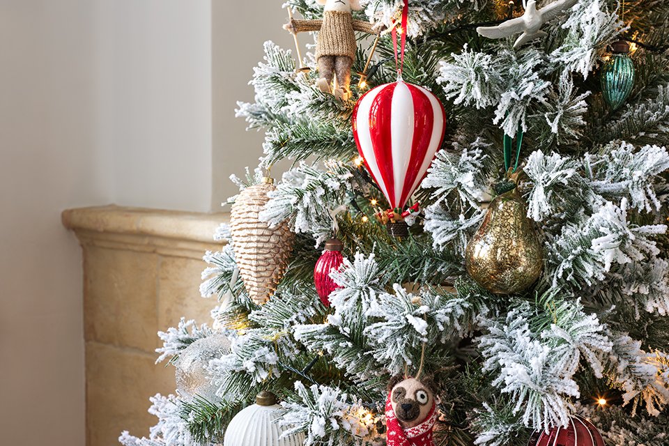 Close up of a forsted christmas tree with red themed baubles hanging on the tree.