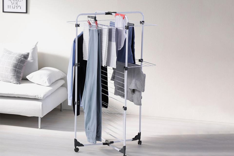 Clothes drying on a wheeled tower airer placed next to a white sofa.