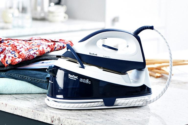 A steam generator iron placed next to a stack of ironed clothes.