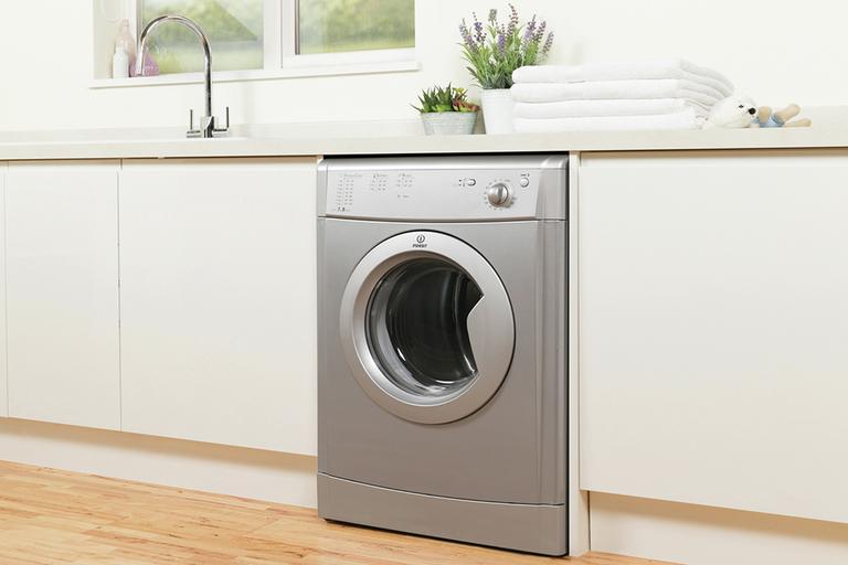 An integrated silver tumble dryer installed in a white utility room unit.