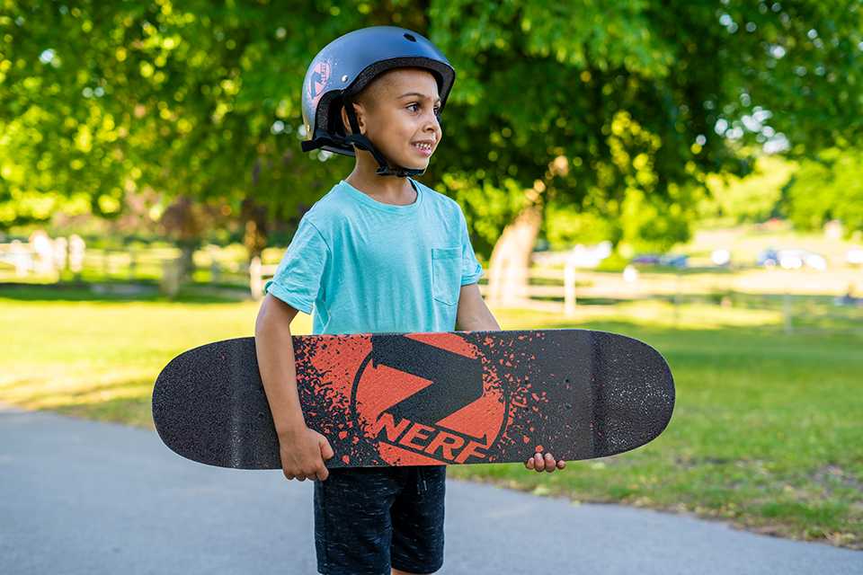 A kid holding a skateboard while wearing a protective helmet.