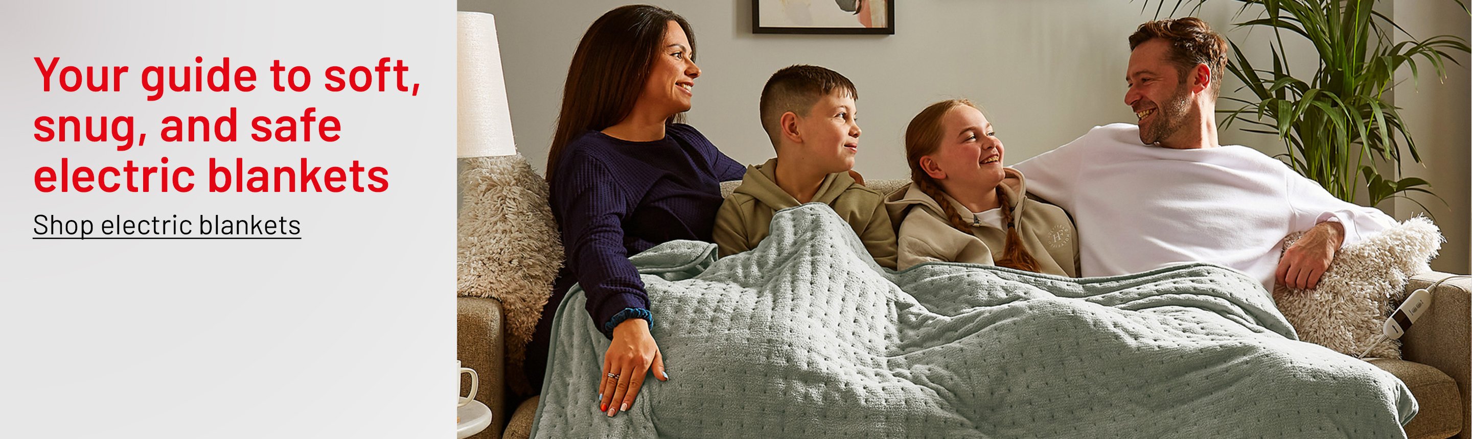 A family of 4 sitting on a sofa with Silentnight Luxury Heated Throw in sage green colour draped over them.