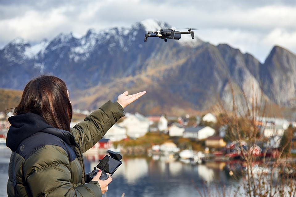 Woman releasing her drone outdoors, near a small village and mountains.
