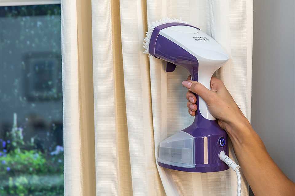 Woman using a handheld vacuum cleaner to clean curtains.