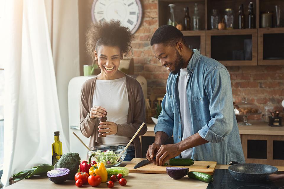 Man and woman laughing and preparing food in kitchen.