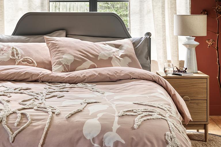 Pink bedding on bed with grey headboard.