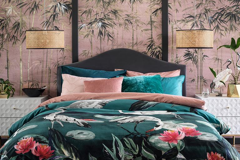 A black bed frame with dark green bedding with pink flamingos.