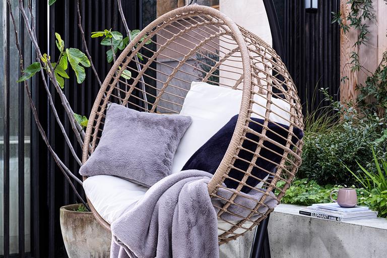 Outdoor egg chair with grey throw and pillow.