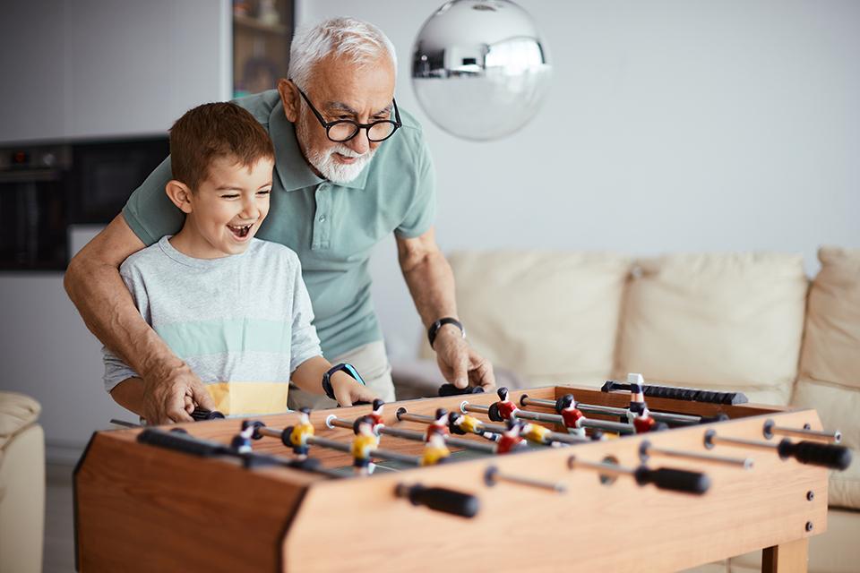 A grandfather teaching his grandson to play table top football.