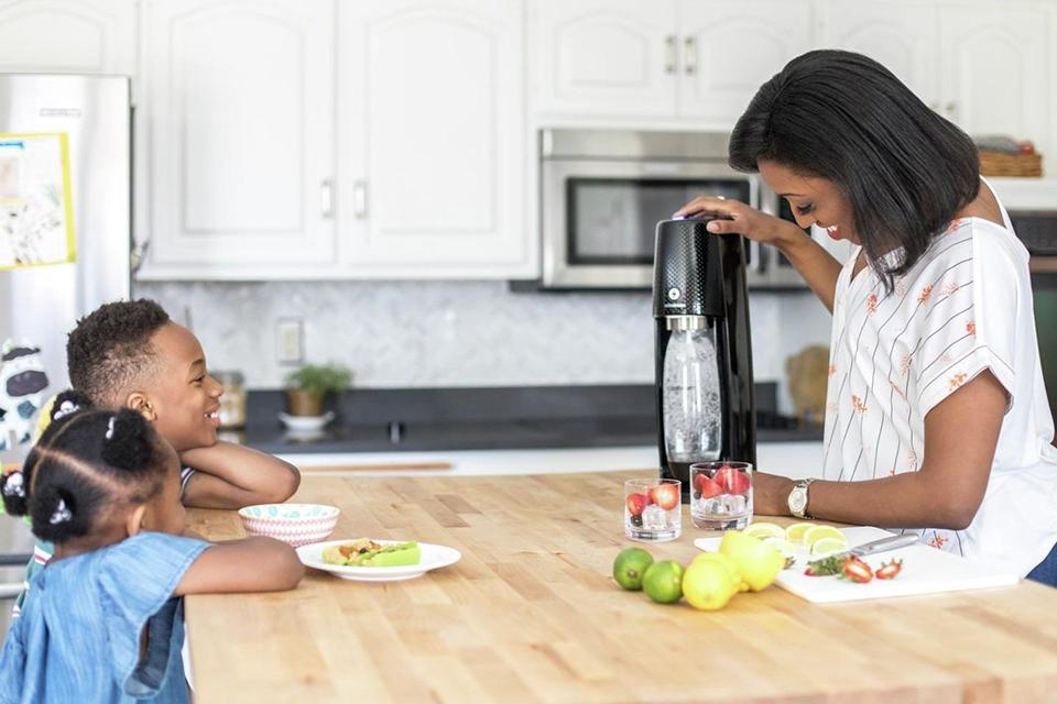 A mother using a SodaStream carbonator in kitchen with her two kids.