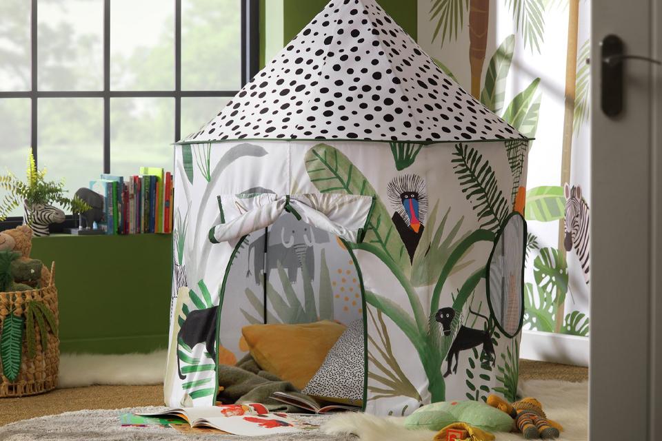 Play tent filled with cushions and blankets in a nature-themed playroom.