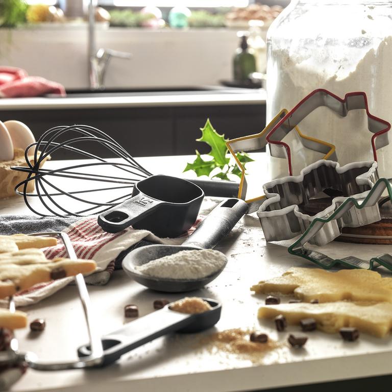 A kitchen counter displaying various baking ingredients and tools such as cookie cutter, measuring spoons, beater, and flour.