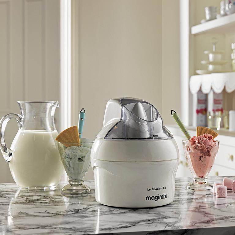 An ice cream maker placed on a kitchen platform next a jug of milk and 2 cups of ice cream.
